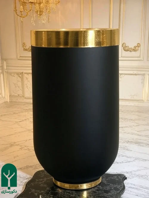 گلدان استوانه ای فایبرگلاس مشکی با لبه استیل طلایی در یک خانه با دیوار های کرم و طلایی با گچ بری سلطنتی
